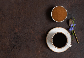 Cup with chicory coffee, chicory powder and blue flowers on a brown background. Space for text. Top view.