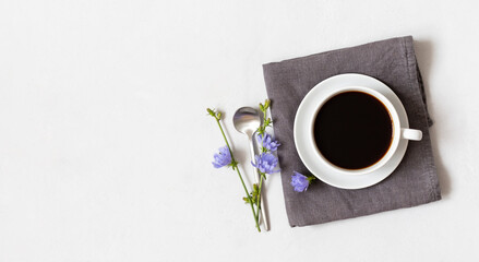Cup with chicory coffee on a gray napkin and blue flowers on a white background. Coffee substitute. Healthy drink. Copy space, top view