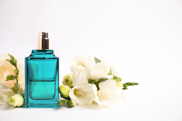 Bottle of perfume and beautiful flowers on white background