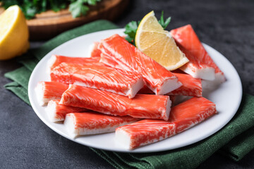 Plate of fresh crab sticks with lemon on grey table, closeup