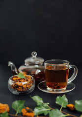 Organic chaga tea on a black background. Infusion with birch mushroom in a glass cup and teapot. Healthy beverage. Vertical orientation.
