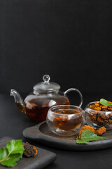 Drink with chaga mushroom in a glass bowl and teapot on a black background. Organic healthy infusion with chaga. Vertical orientation.