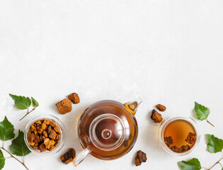 Obraz na płótnie Canvas Chaga tea in glass bowls and teapot, chaga mushroom pieces, birch leaves on a white background. Space for text. Top view, flat lay.