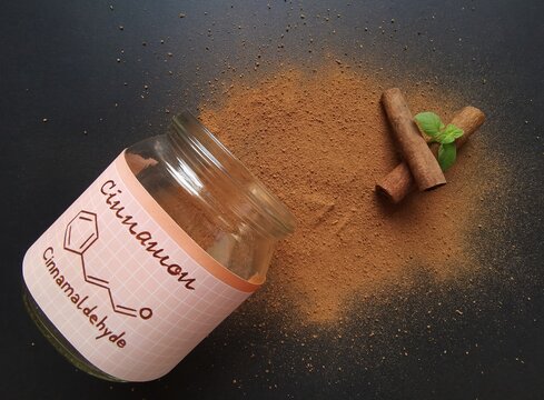 Cinnamon sticks and milled cinnamon spice in the glass jar with structural chemical formula of cinnamaldehyde (the major component of cinnamon). Winter spices, cinnamon sticks and cinnamon powder.