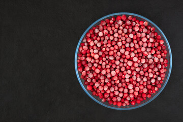 Frozen cranberries in a large plate on a black background. Red frozen berries in a glass bowl. Copy space. Top view, flat lay.