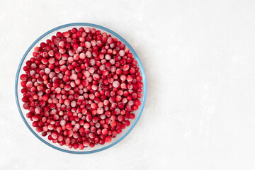 Frozen cranberry berries in a large transparent plate on a white background. Vitamins. Copy space, top view, flat lay.