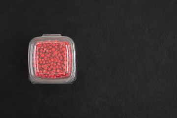 Plastic container with frozen red currant berries on a black background. Copy space, top view.