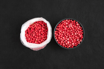 Frozen red berries on a black background. Red currant in a bag and bowl. Vegetarian food. Top view, flat lay.