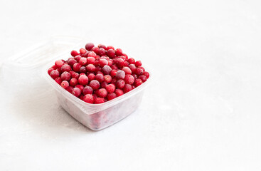 Frozen cranberry berries in a plastic container on a white background. Vitamins. Copy space.