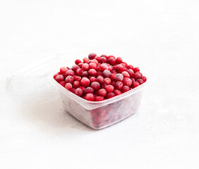 Frozen cranberries in a plastic container on a white background. Storage of frozen food.