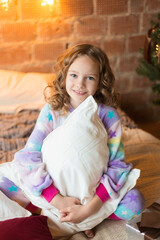 Cute little girl sits on the bed and huggs pillows with background of tree