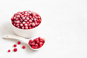 Frozen red berries in a bowl with a spoon on a white background. Cranberries with frost. Vegetarian food. Space for text.