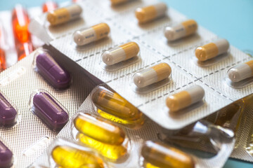 Orange and yellow capsules pill in blister. Purple and green tablets on blue background. Antimicrobial capsule pills. Pharmaceutical industry. Pharmacy.