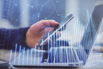 Double exposure of man's hands holding and using a phone and financial graph drawing. Analysis concept.