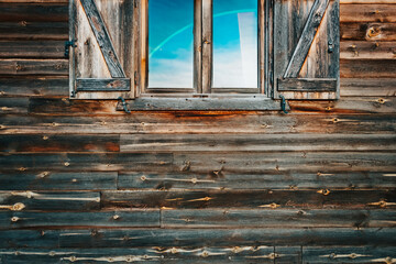 Background of the facade of a wooden wall with a window with open shutters and blue glass.