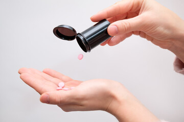 Female hands with prescription medicines on gray background. Woman taking vitamins and supplements. An unrecognizable woman pours several vitamins into her hand. She takes the vitamins daily.