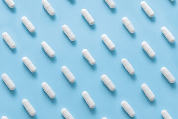 Scattered Pills on a blue background , Medicine concept. Multiple long white capsules on a blue. Pattern of capsules on a blue. Minimalism background