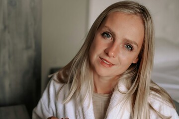 Naklejka premium A portrait of a beautiful young blondie woman. A girl in a white bathrobe looks at the camera.