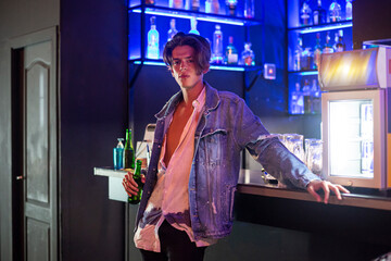 Close-up portrait of young man with a beer and jean jacket with bar background.
