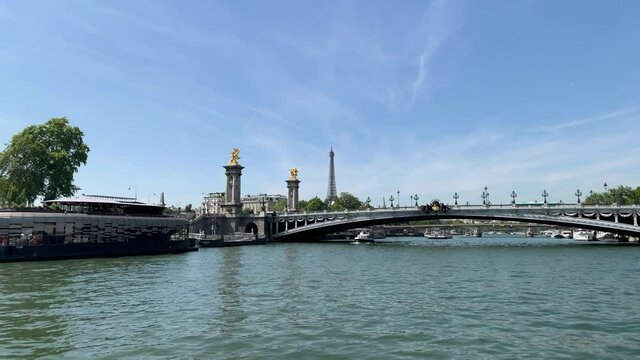 Footage of boats on Seine river, bridge called "Pont Alexandre III" and Eiffel tower (landmark and cultural icon) in Paris. It is a sunny summer day. Camera moves forward.
