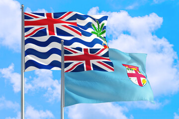Fototapeta na wymiar Fiji and British Indian Ocean Territory national flag waving in blue sky. Diplomacy and international relations concept.