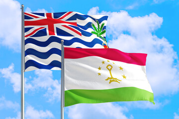 Tajikistan and British Indian Ocean Territory national flag waving in blue sky. Diplomacy and international relations concept.