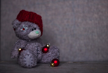 cute cristmas teddy bear in red shining knitted hat, with several red balls is sitting on wooden table, merry christmas and happy new year,  card, copy space, congratulations, banner