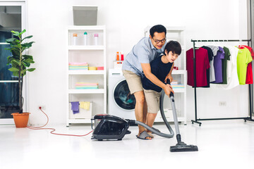 Fototapeta premium Father teaching asian kid little boy son having fun doing household chores cleaning and washing floor wiping dust with vacuum cleaner while cleaning house together at home.Housework concept