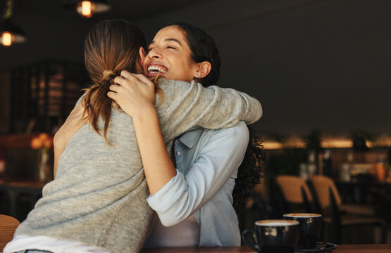 Female friends greeting each other with a hug in a cafe