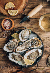 Fototapeta premium Fresh oysters with ice and lemon on a rustic wooden background.