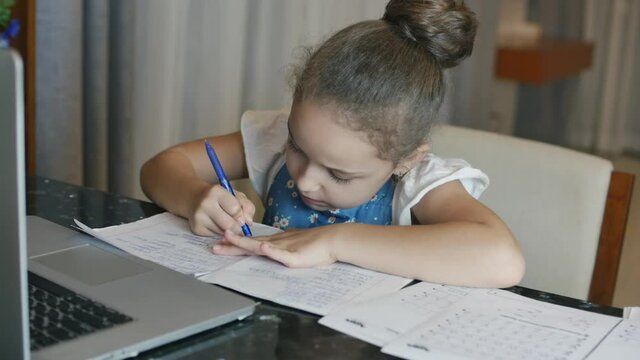 little girl a cute elementary school child of 7-8 years old at home studying in family learning listens to school lectures does homework without leaving home.Child homeschooling,kids education concept