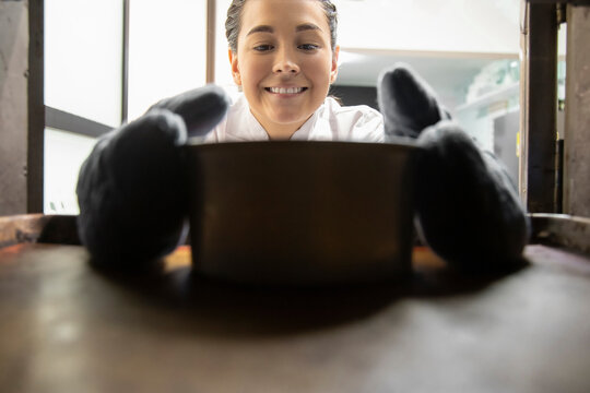 Smiling Young Woman With Oven Mitts Taking A Cake Out Of The Oven