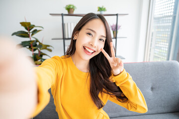 Pretty young asian female with big smile sitting at living room. She having fun taking light cheerful selfie on blurred background