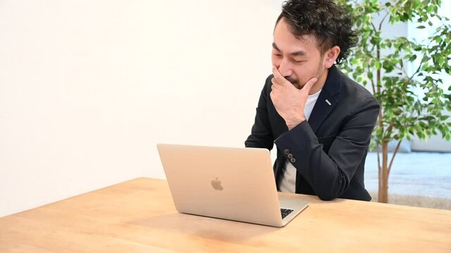  パソコンの前こんなはずではなかったのにと笑いながらリモートで会話する若い日本人男性の動画