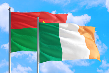 Ireland and Burkina Faso national flag waving in the windy deep blue sky. Diplomacy and international relations concept.
