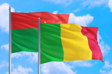 Mali and Burkina Faso national flag waving in the windy deep blue sky. Diplomacy and international relations concept.