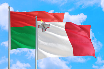 Malta and Burkina Faso national flag waving in the windy deep blue sky. Diplomacy and international relations concept.