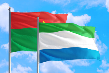 Fototapeta na wymiar Sierra Leone and Burkina Faso national flag waving in the windy deep blue sky. Diplomacy and international relations concept.