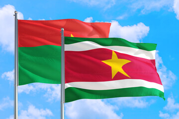 Fototapeta na wymiar Suriname and Burkina Faso national flag waving in the windy deep blue sky. Diplomacy and international relations concept.