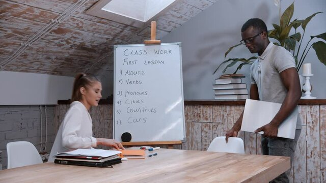 Woman english teacher waiting for her student - an african-american man walks in the class and the teacher starts cleaning up the board
