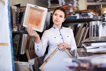 Happy positive smiling woman is choosing new picture for her home in the store.