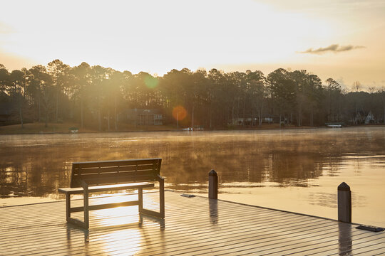 Bench on the dock of the lake at sunrise with cool water and warm air