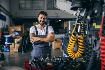 Fototapeta Smiling happy bearded tattooed worker in overalls standing next to truck with arms crossed. obraz