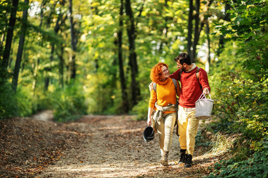 Young happy couple in love hugging and walking in nature. Couple is holding picnic equipment.