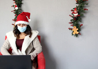 
Latin woman with protection mask and Santa Claus hat on video call with cell phone and laptop....