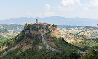 Fototapeta na wymiar Cività di Bagnoregio sitting on a limestone cliff and slowly decaying. A medieval town center with a church and old houses holds on the plateau among a scenic eroded landscape