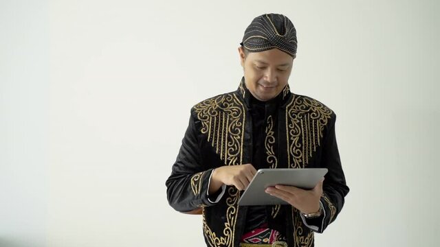 happy traditional Javanese man holding a tablet wearing beskap