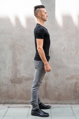 Full length profile view shot of handsome young Italian man standing against gray wall outdoors