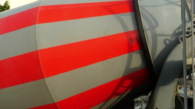 A grey and red concrete mixer turns in the morning sun