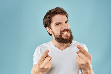 Bearded man in white T-shirt emotions gestures with hands displeased facial expression blue background